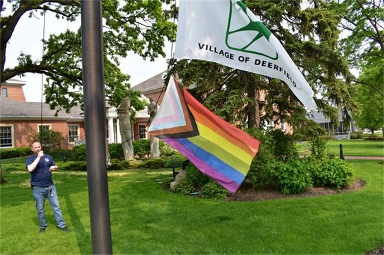 A man raises the LGBTQ Progress Pride flag at Village Hall.
