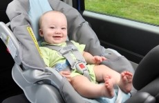 A baby sits smiling in a car seat
